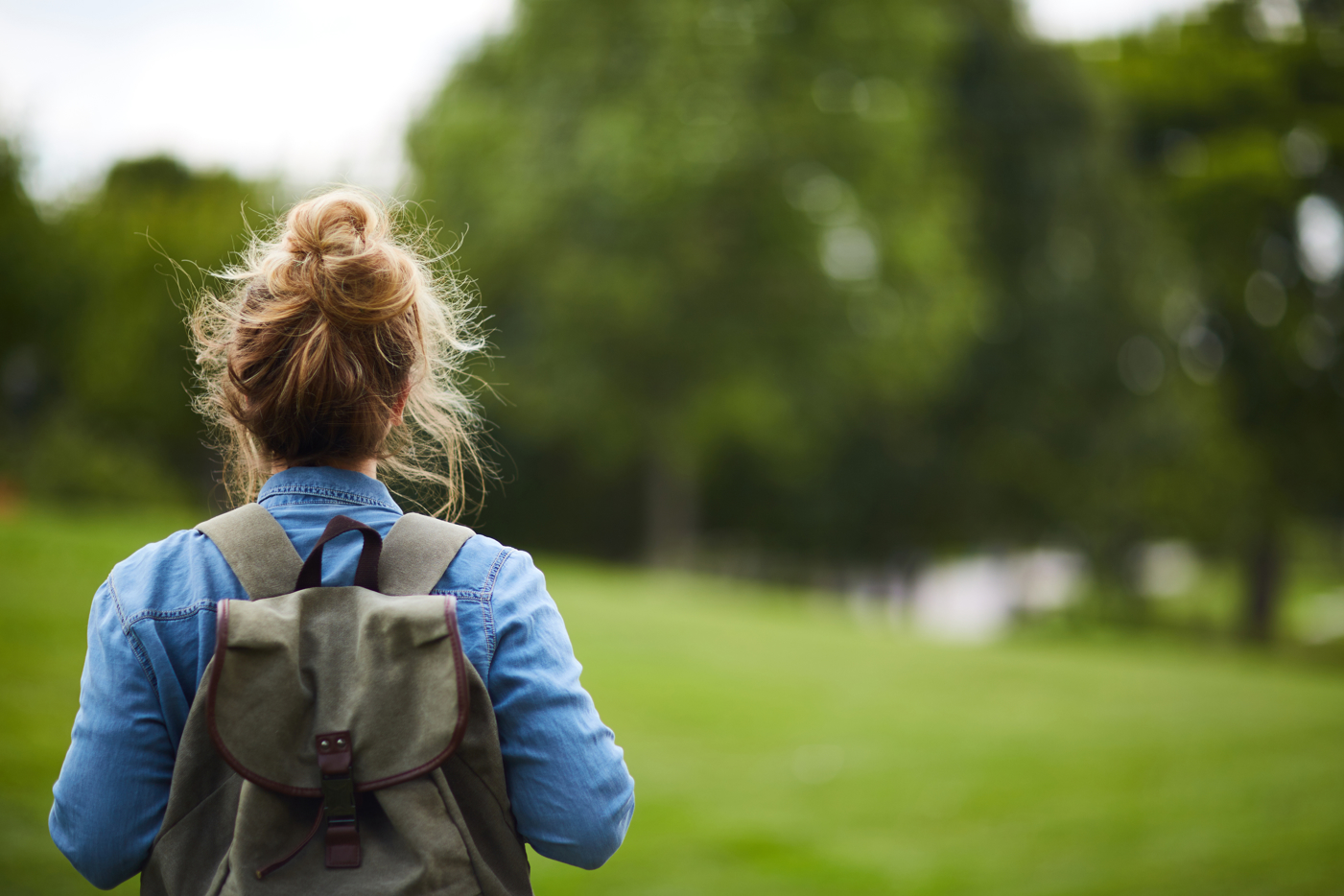 Rear view of a woman with rucksack on a walk in a green park