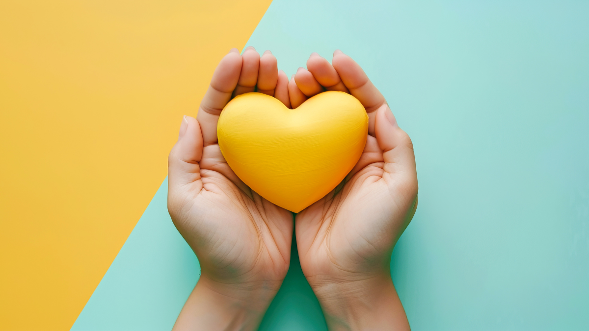 a yellow wooden heart cupped in two hands, with a yellow and turquoise background